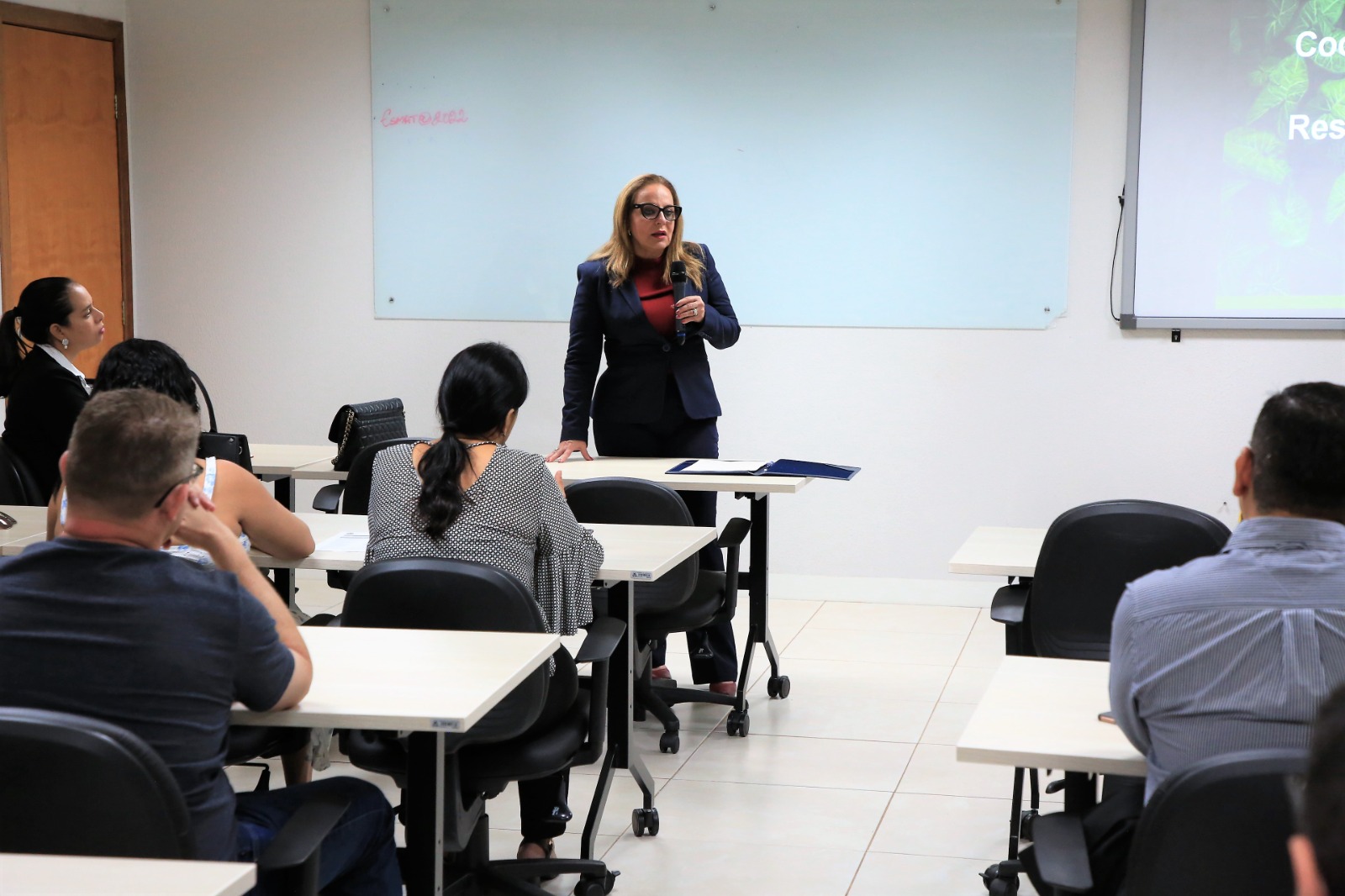 Em pé, de roupa preta, desembargadora Ângela ministra workshop a servidores sentados