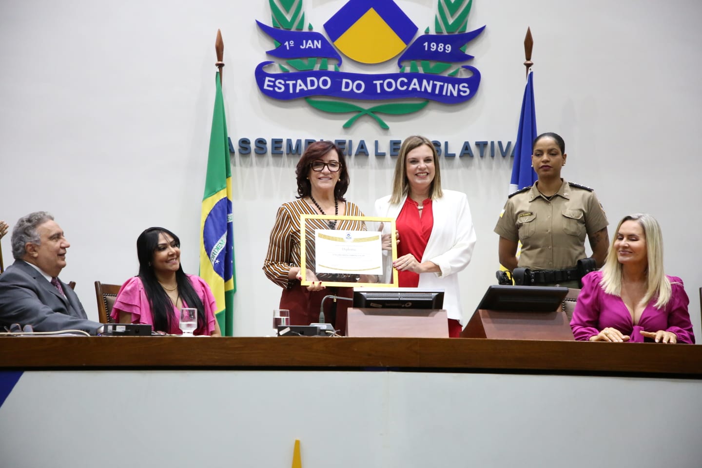 Imagem tem cinco pessoas, três sentadas,  em pés estão a presidente do TJTO e a deputada estadual Cláudia Lelis