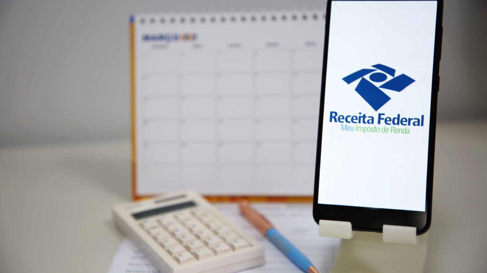 Imagem com calculadora, celular, caneta e calendário para falar sobre comprovante de rendimentos para IRPF