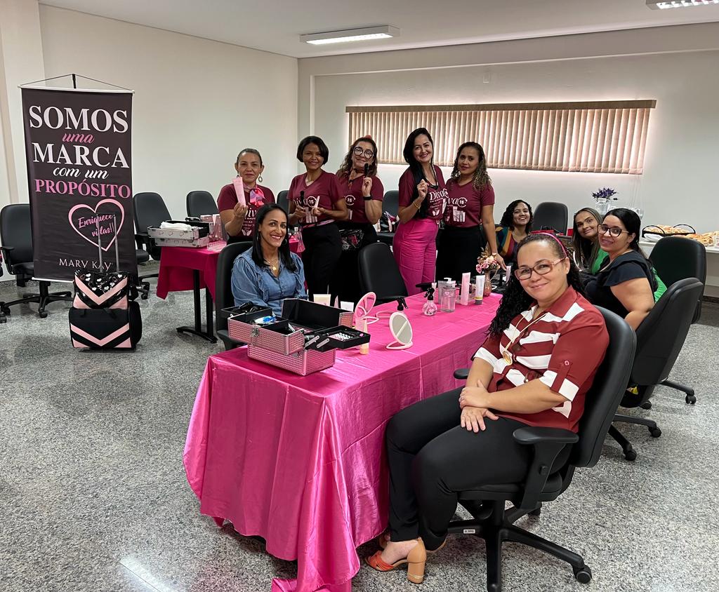 Imagem com várias mulheres sentadas em uma mesa com toalha rosa durante curso de maquiagem e autocuidado