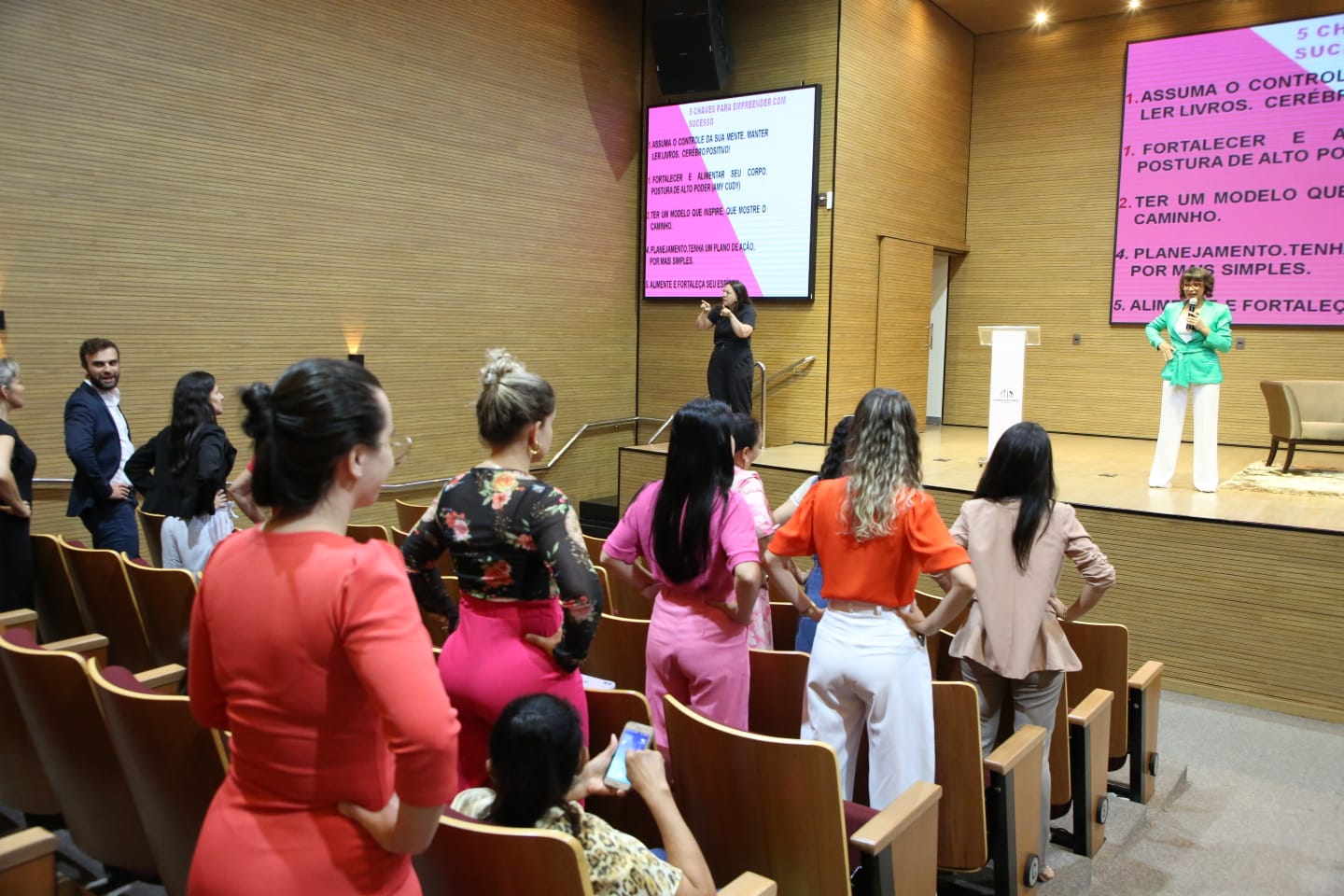 Auditório com mulheres em pé e palestrante à frente falando sobre empreendedorismo