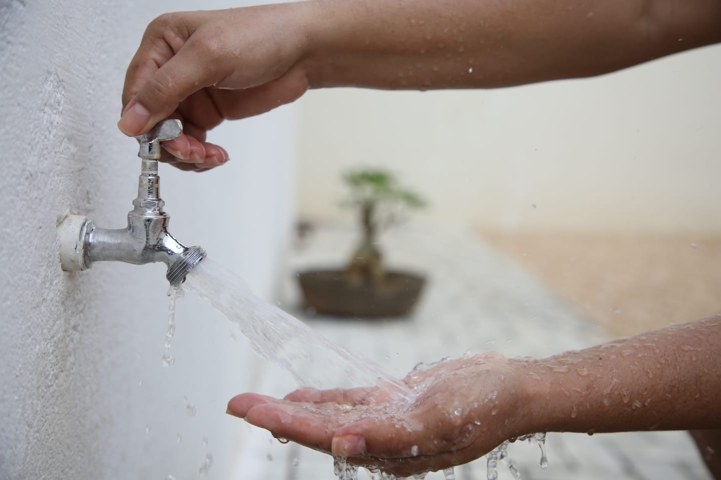Imagem de uma pessoa abrindo a torneira e lavando as mãos