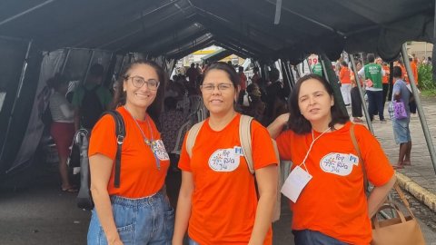Três mulheres com blusas laranjadas participam do mutirão Pop Rua Jud em Recife