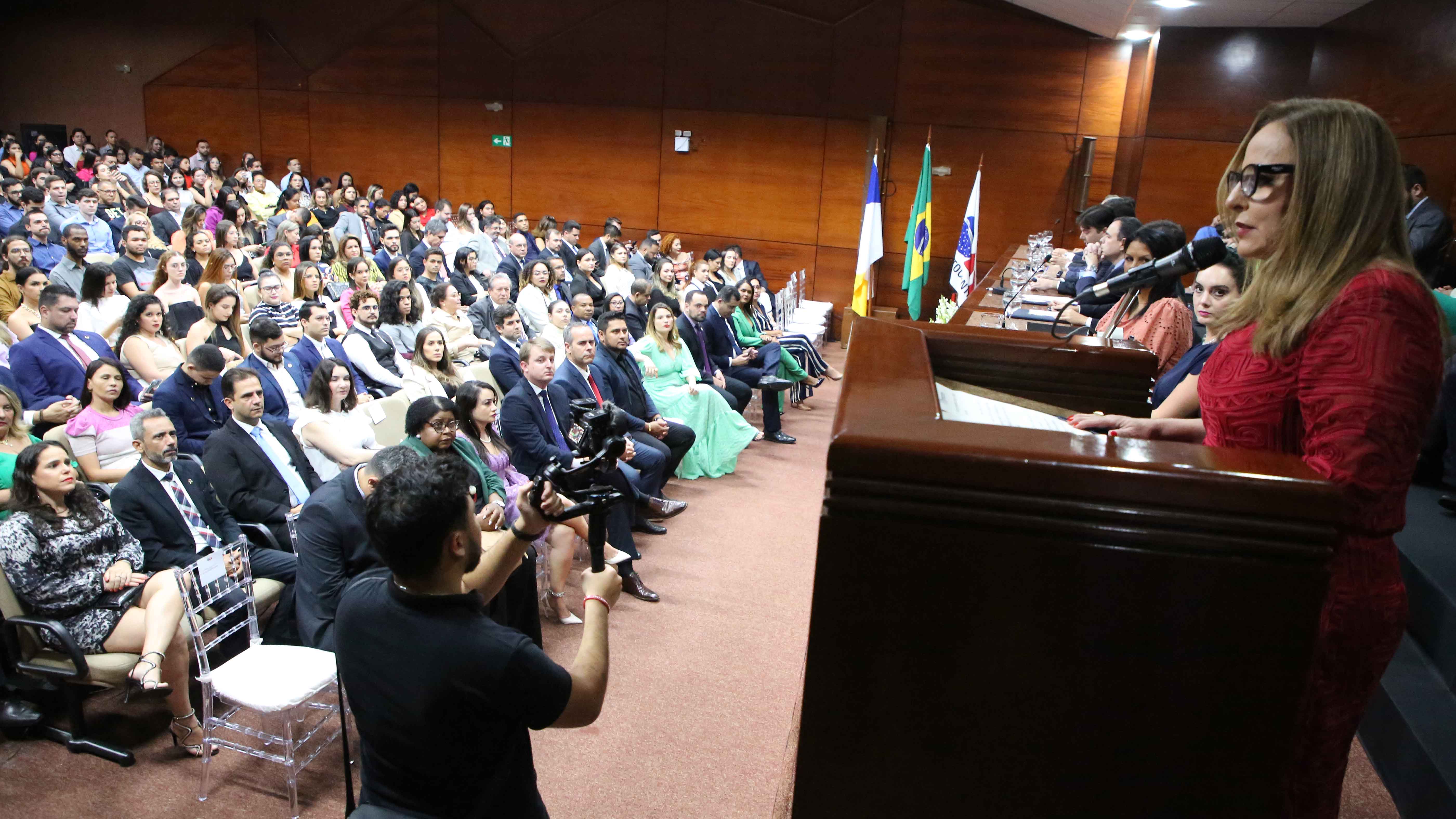Imagem mostra auditório com bastante gente e no púlpito aparece a desembargadora Ângela Prudente fazendo pronunciamento
