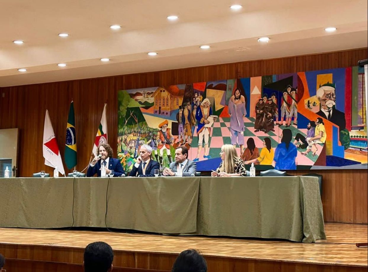 Juiz Océlio Nobre discursando sentado em uma mesa ao lado de outras três autoridades que também participaram do debate