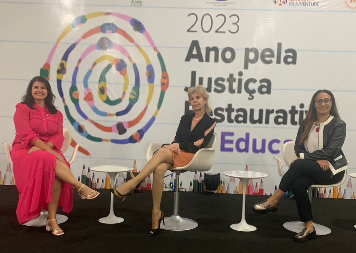magistradas tocantinenses posam para foto sentadas em uma cadeira a frente de um banner com escrita "2023 Ano pela Justiça Restaurativa"