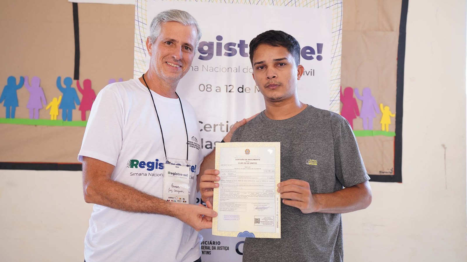 Voluntário da ação e homem beneficiado posando para a foto segurando certidão de nascimento