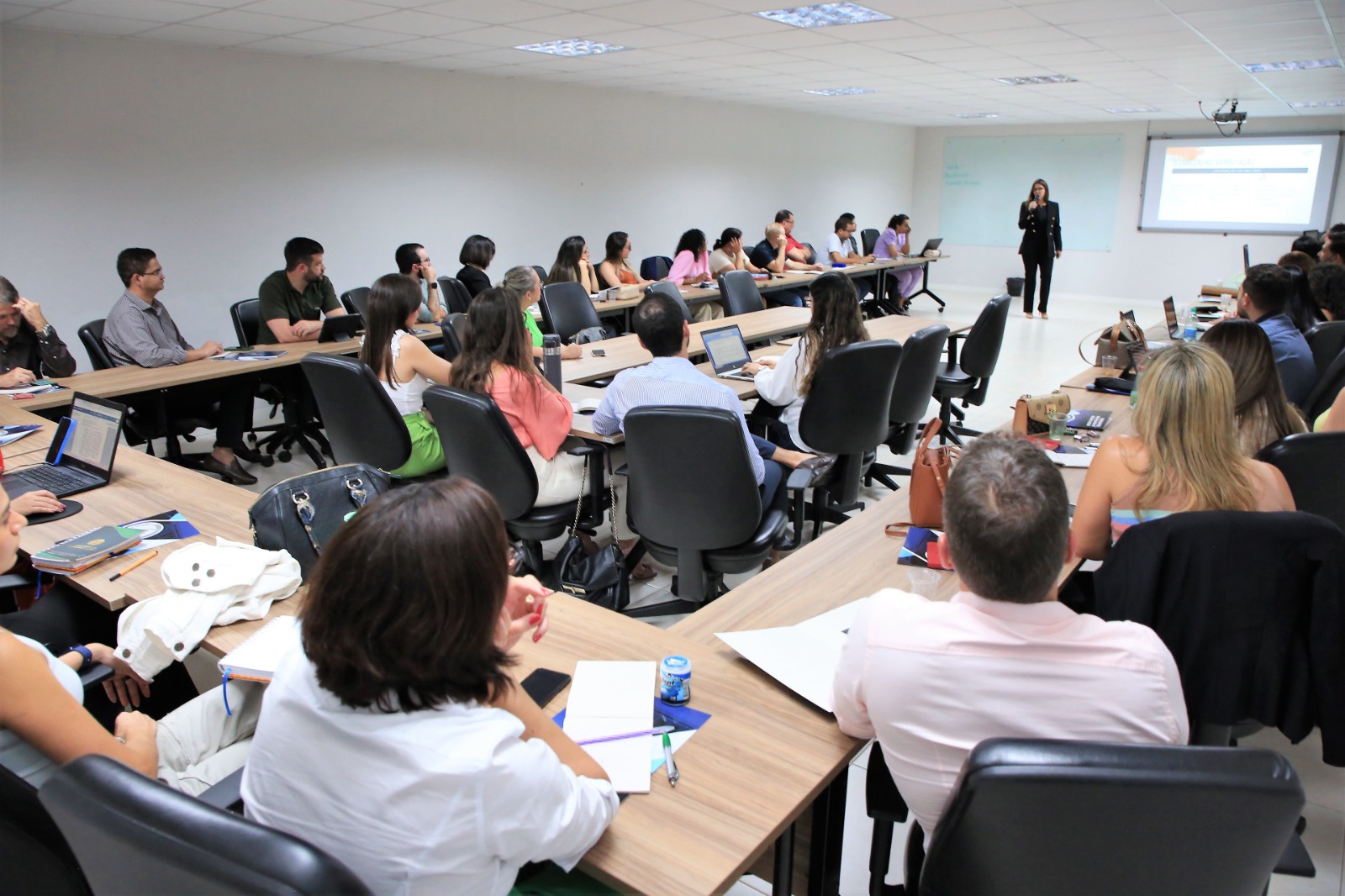 participantes do curso sentados em meia lua olhando atentamente a apresentação de slides