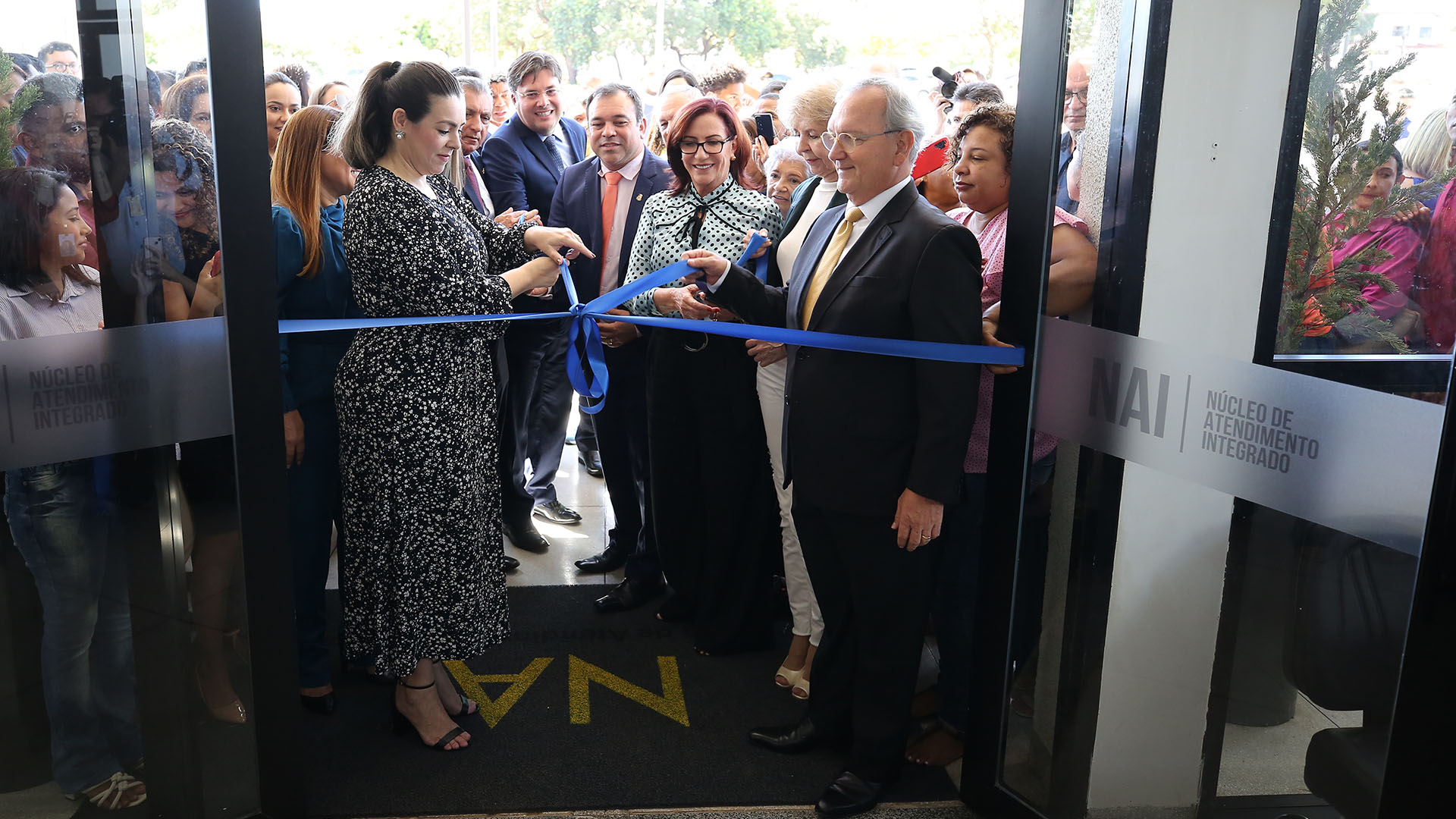 Fotografia colorida de autoridades descerrando cortando a faixa de  inauguração do NAI