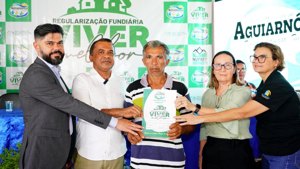 Servidores e desembargadora Maysa Vendramini segurando título de propriedade juntamente ao beneficiado e posando para foto
