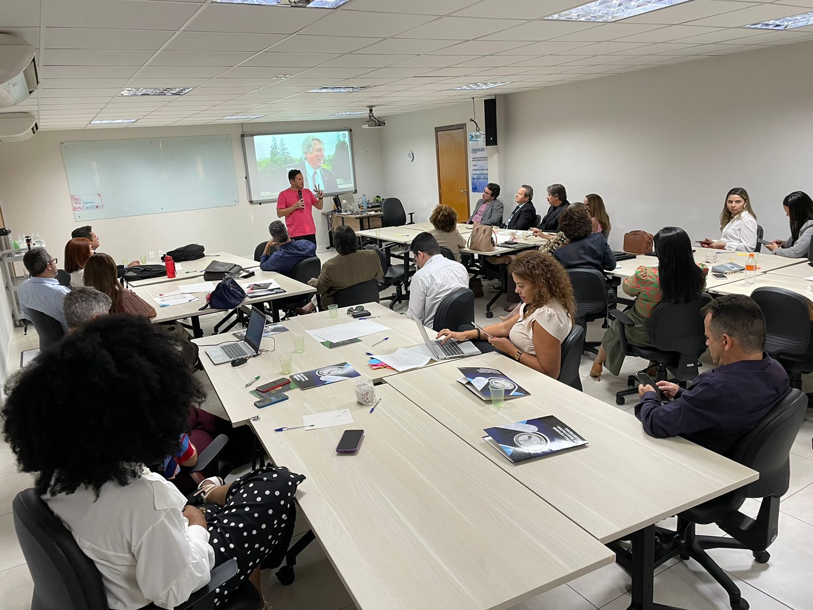 Foto mostra várias pessoas sentadas em uma sala e o publicitário André Tamura falando sobre o processo de inovação