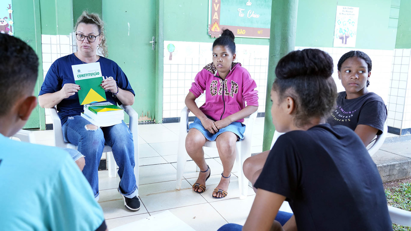 alunos em roda observam um homem que segura uma cópia da constituição