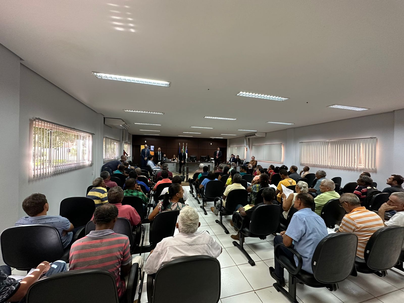 Imagem colorida que mostra uma sala lotada de pessoas sentadas obser