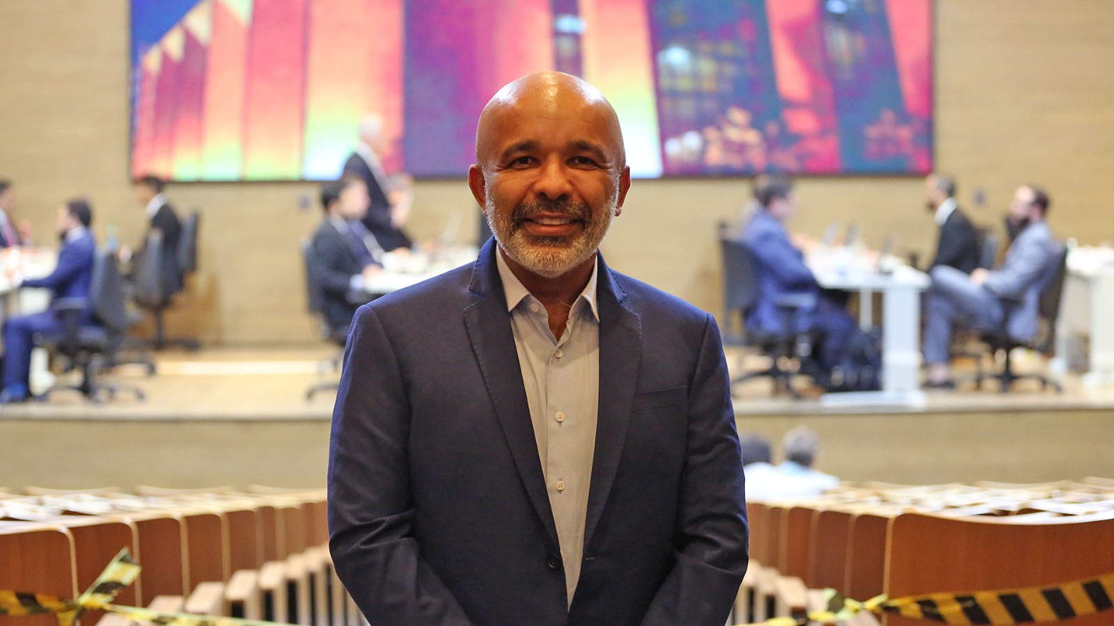 Homem negro, careca, usando um terno sorri para a foto