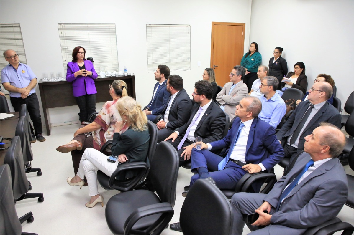 Imagem mostra homens e mulheres em pé, ao fundo parede branca com porta de correr em madeira 