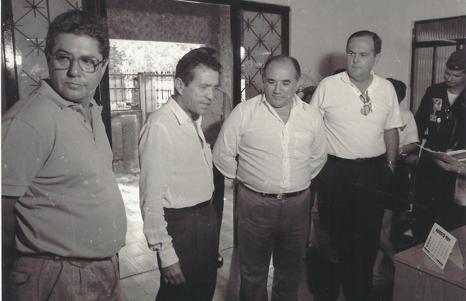 Fotografia em preto e branco que mostra homens posando para a imagem dentro de uma sala