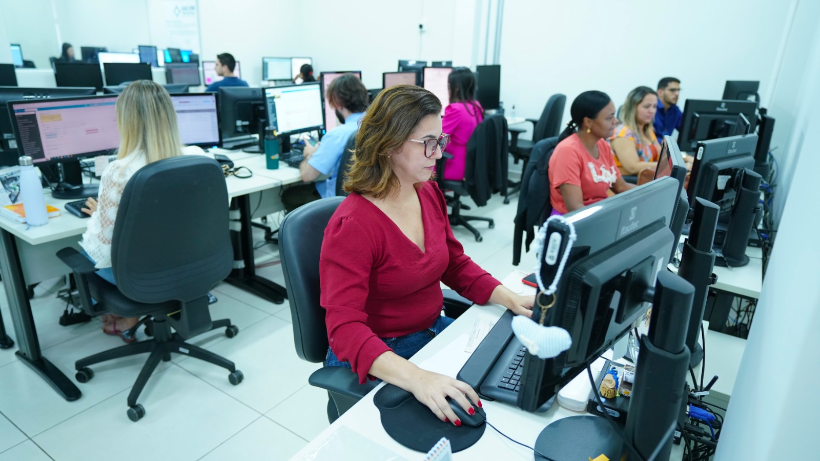 Equipe do Nacom trabalhando em uma sala com vários computadores, estantes e papeis