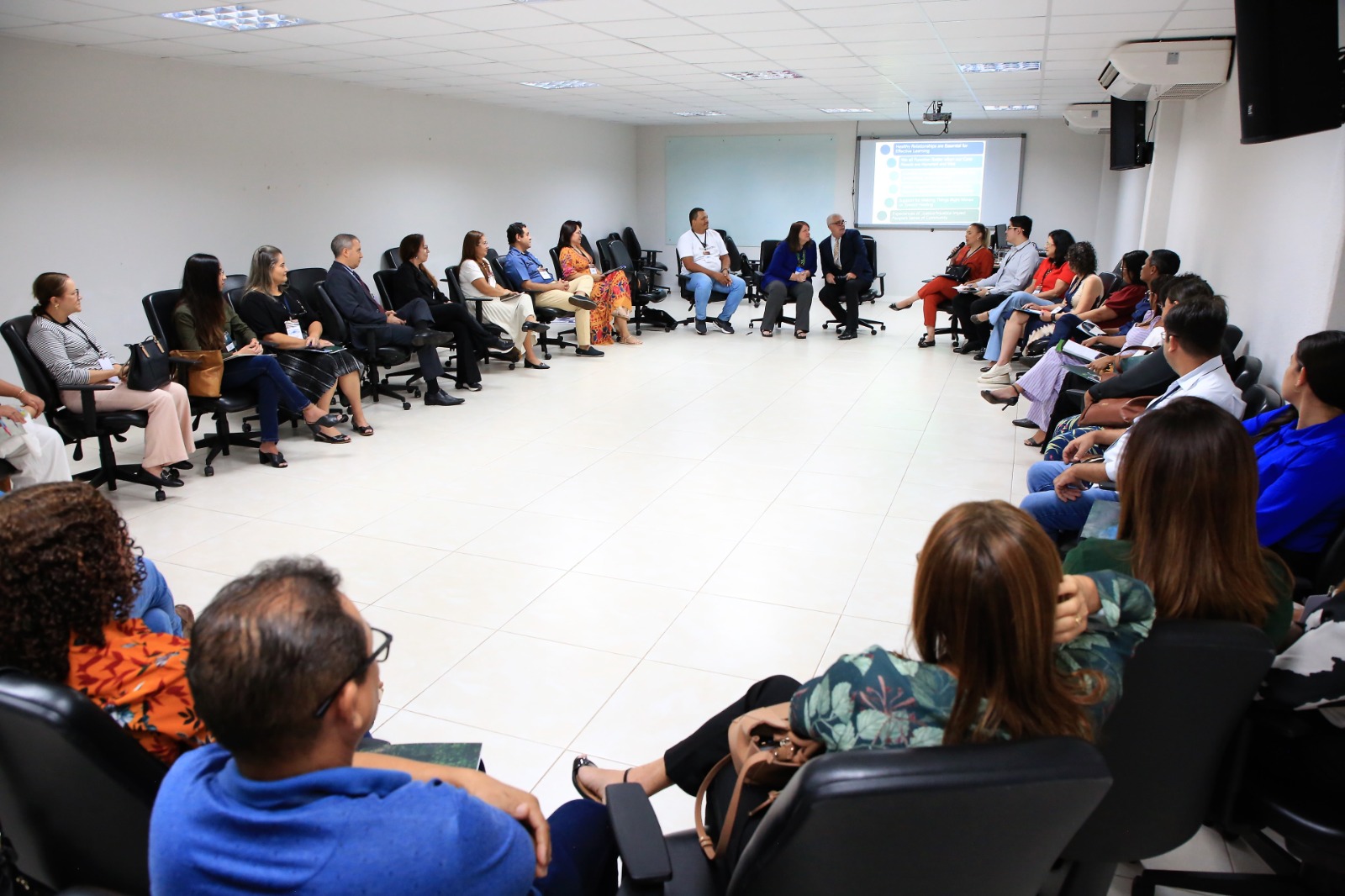 Imagem mostram várias pessoas sentadas em um círculo dentro de uma sala da Esmat