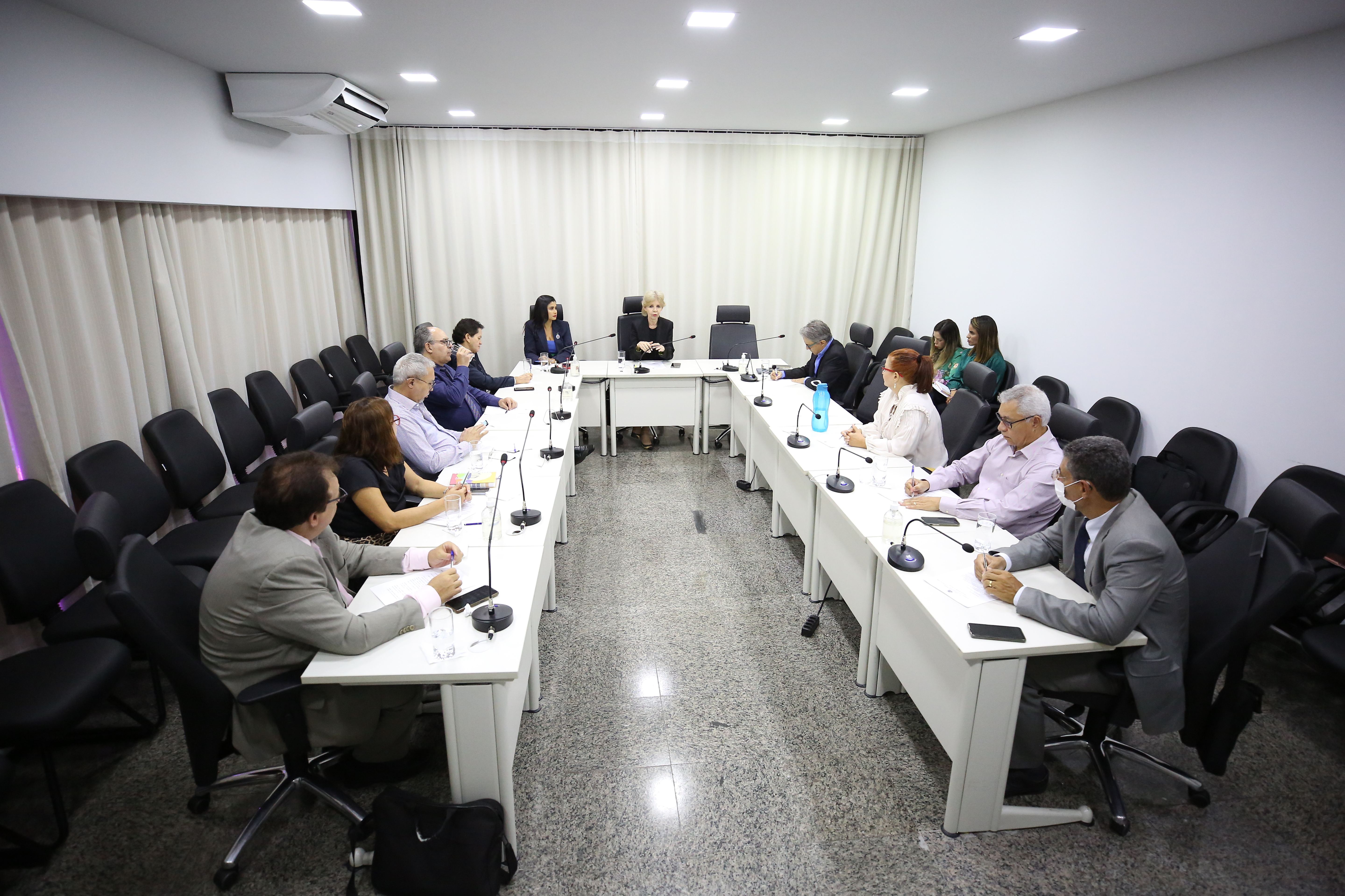 Homens e mulheres sentados em volta de uma mesa em U de cor branca durante reunião