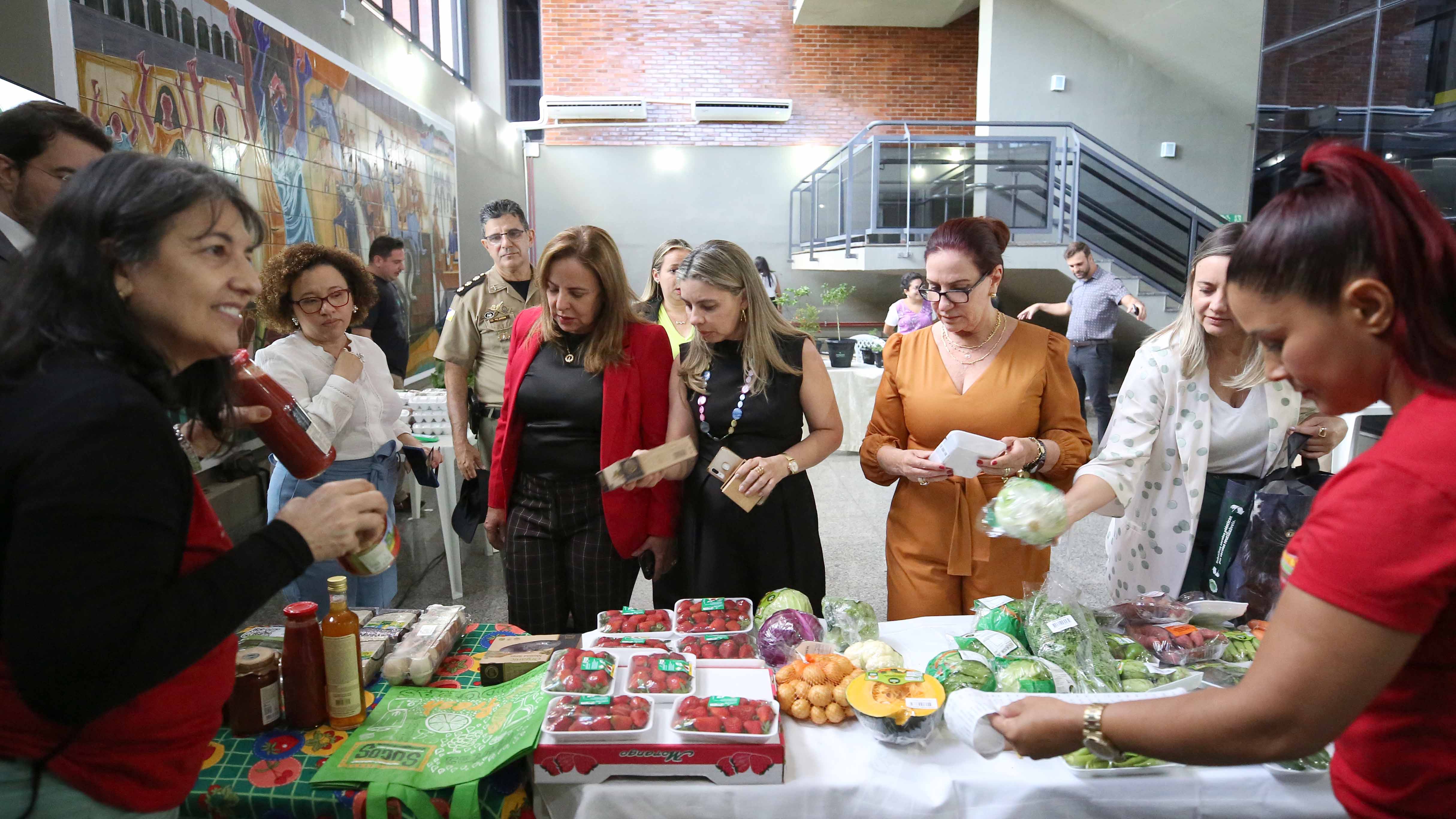 Imagem colorida que mostram mulheres escolhendo produtos na feira Ecosolidária
