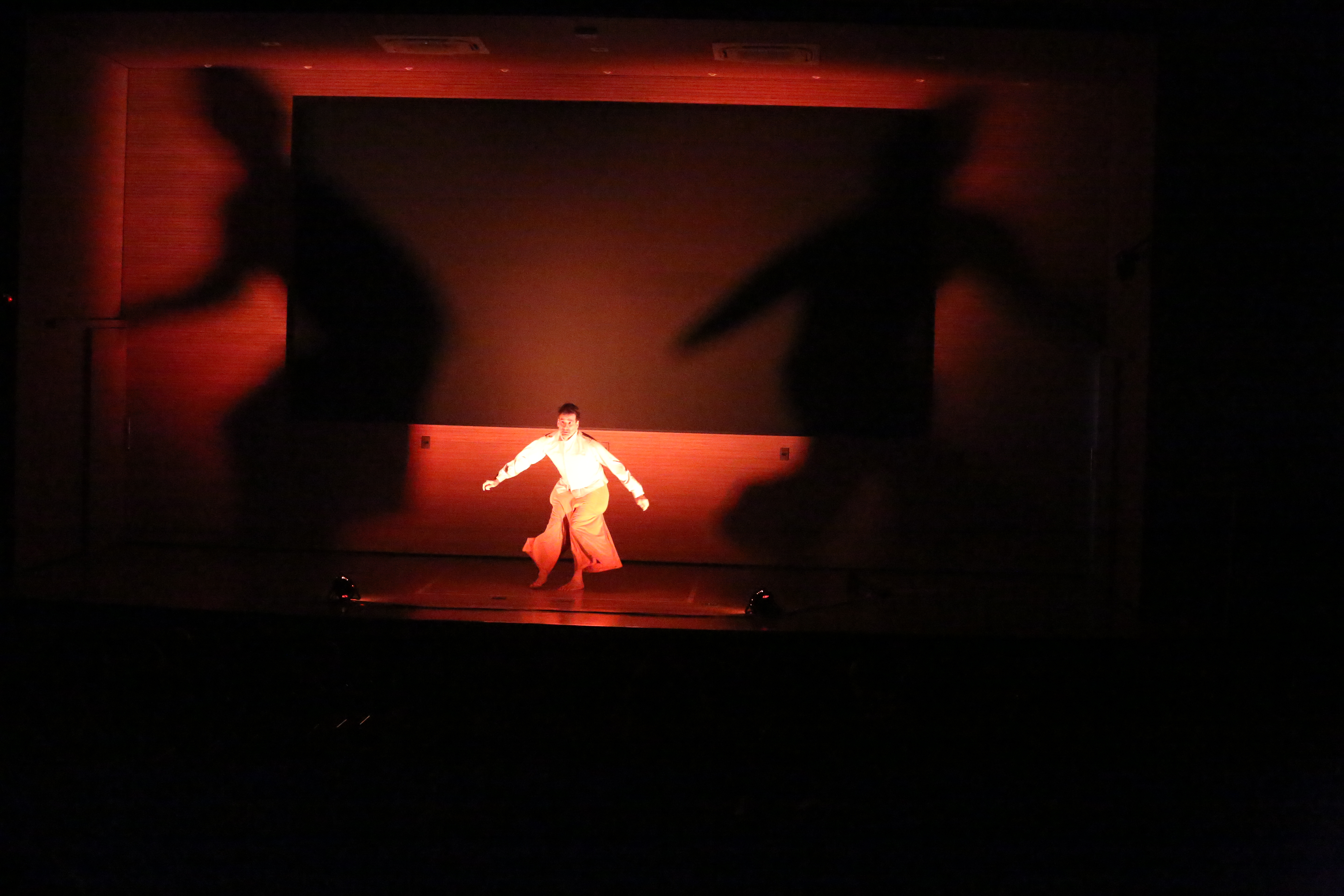 Homem no palco encena sob luz vermelha e contornado por sombras