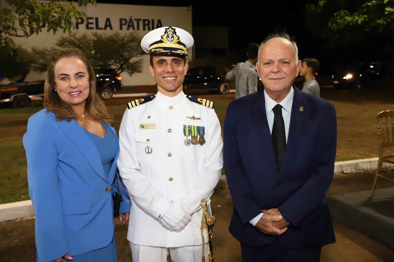 Mulher vestindo azul posa ao lado de marinheiro de farda e de homem vestindo terno