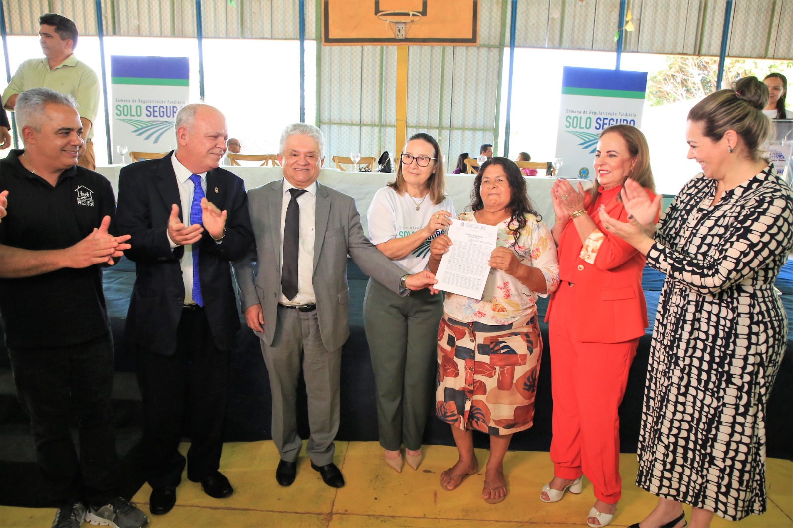 Homens e mulheres aplaudem uma senhora segurando um documento