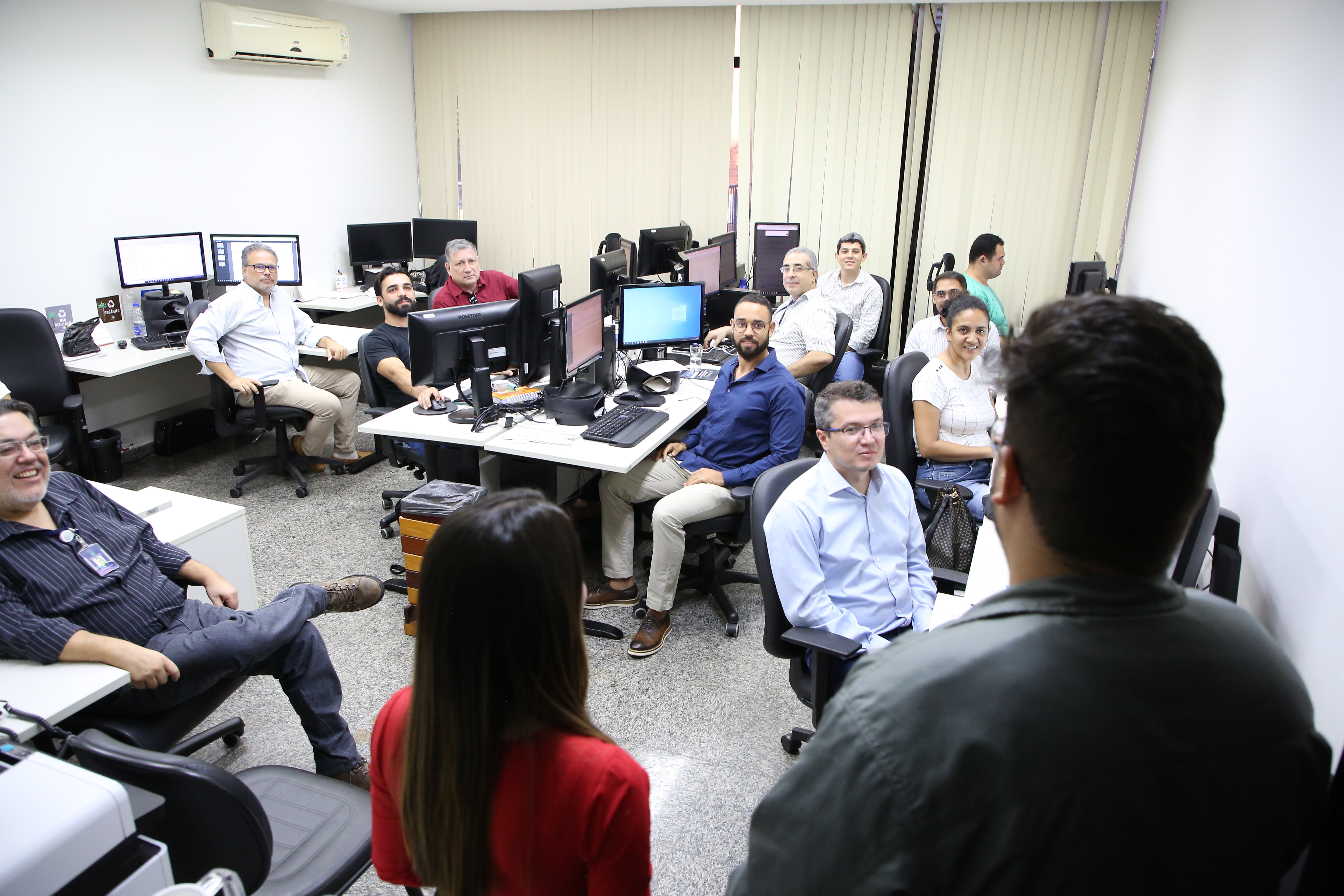 duas pessoas em pé (de costas para foto) conversando com servidores que estão sentados e olhando atentamente as pessoas que estão falando