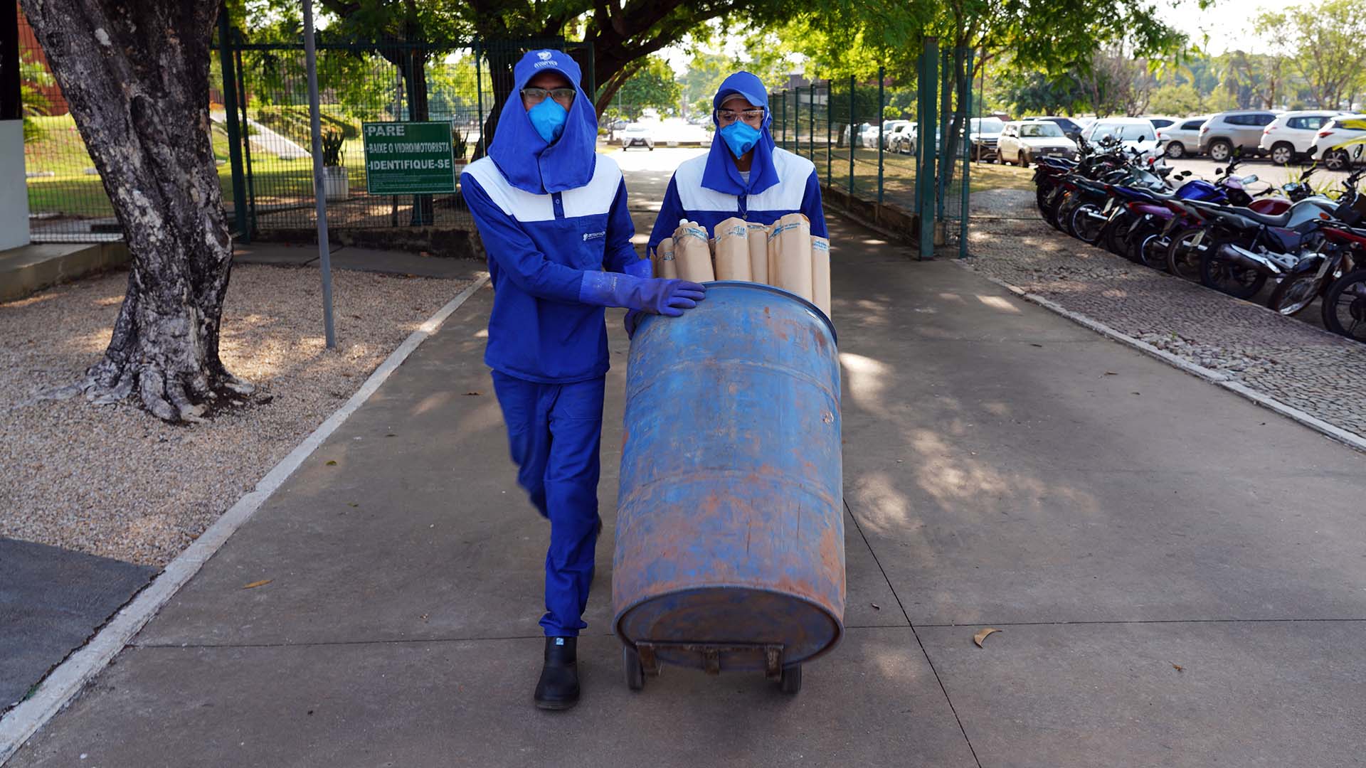 Homens com equipamentos de proteção individual carregando tambor com diversas lâmpadas dentro