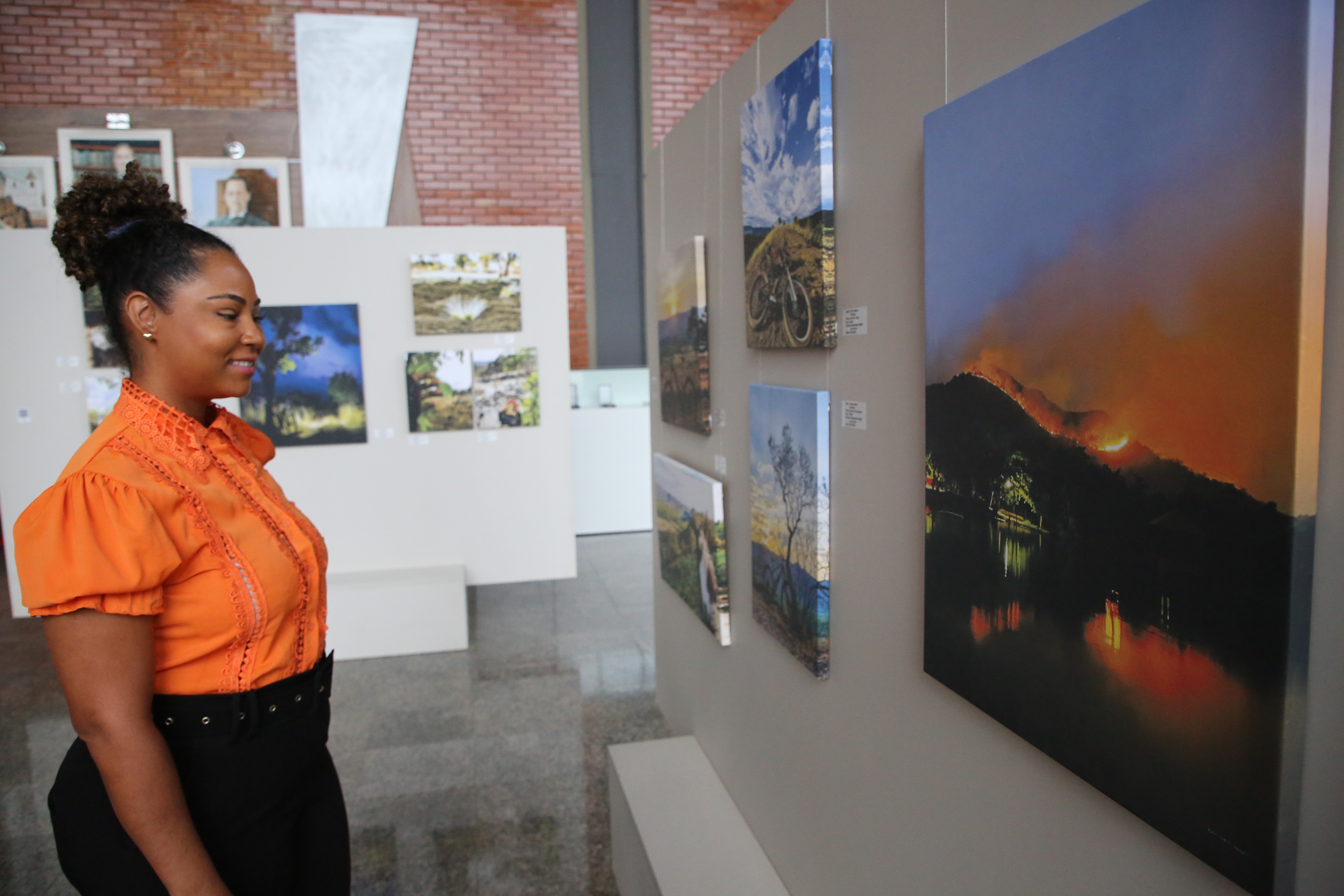 Mulher negra vestindo laranja e preto olha para um quadro de por do sol