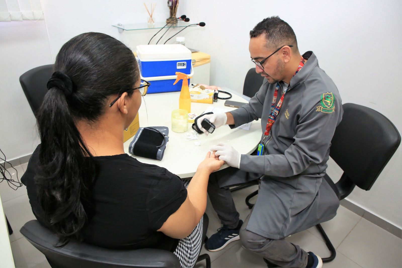 enfermeiro de jaleco cinza realiza atendimento a mulher que veste blusa preta