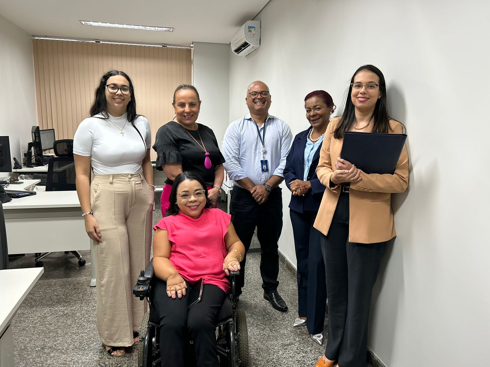 pessoas em pé junto com uma pessoa com deficiência em cadeiras de rodas reunidas e posando para foto