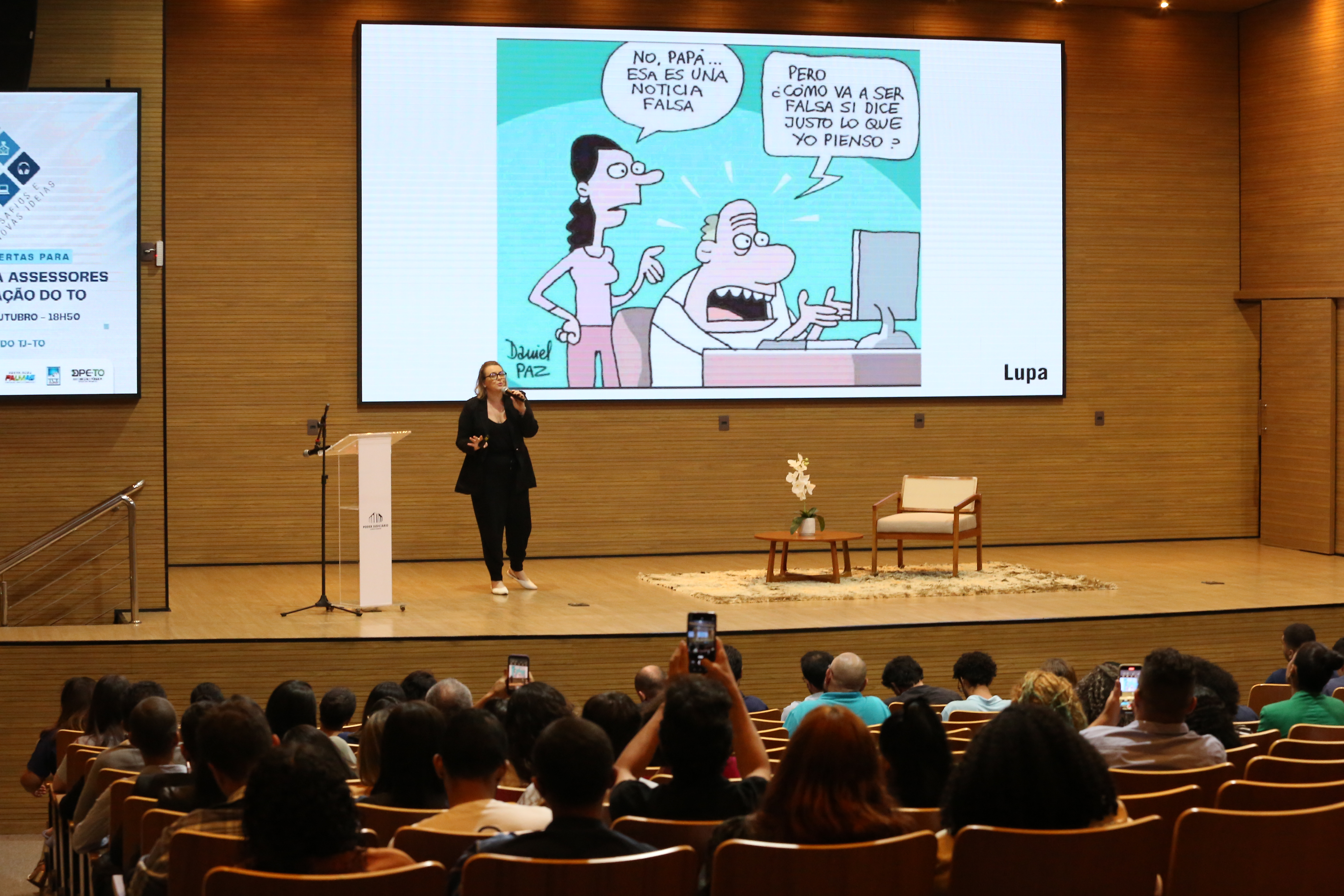 CEO da Agência Lupa palestrando para o público com slide projetado às suas costas contendo uma tirinha sarcástica