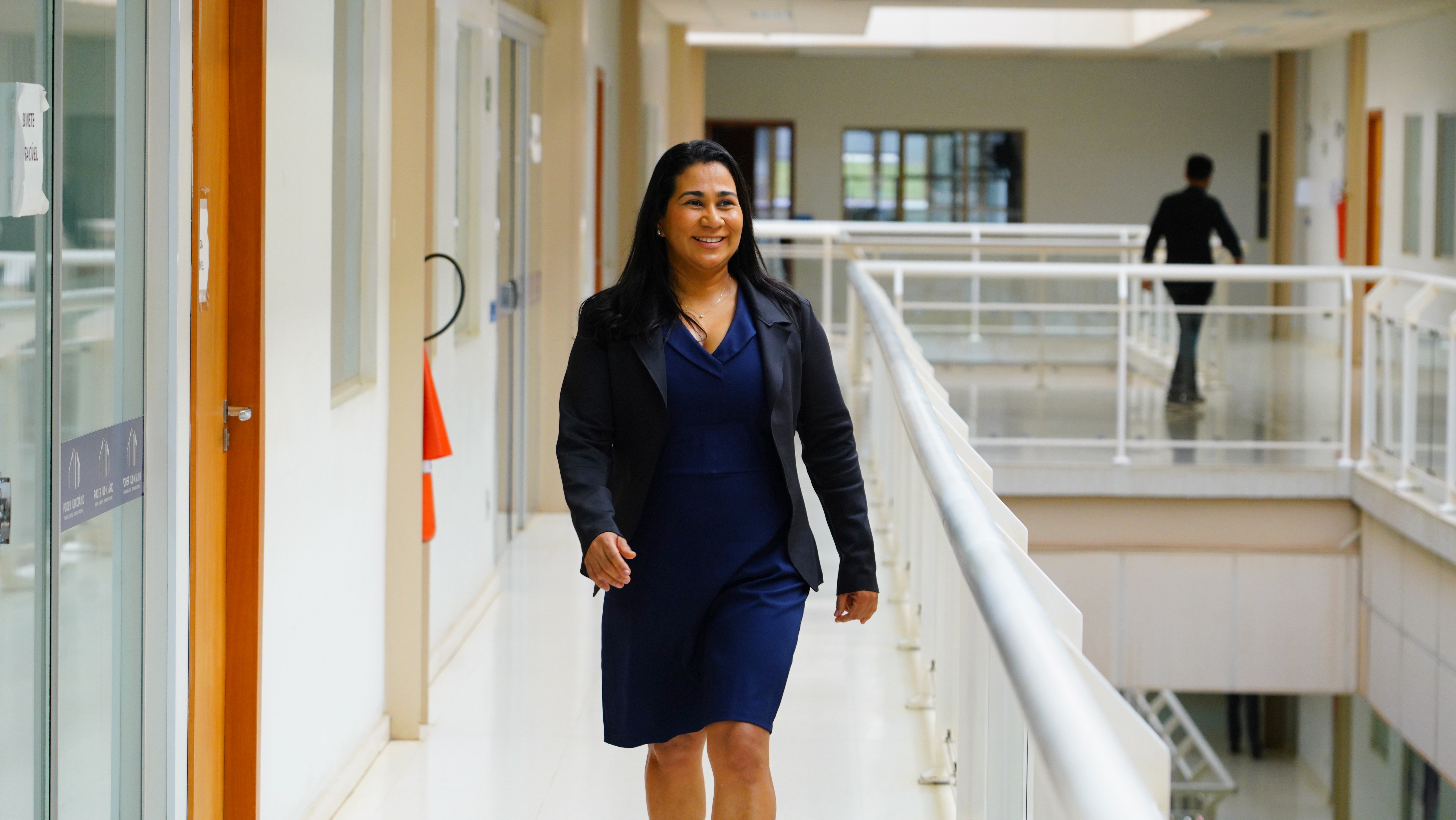 Mulher morena vestindo azul caminha dentro do Fórum