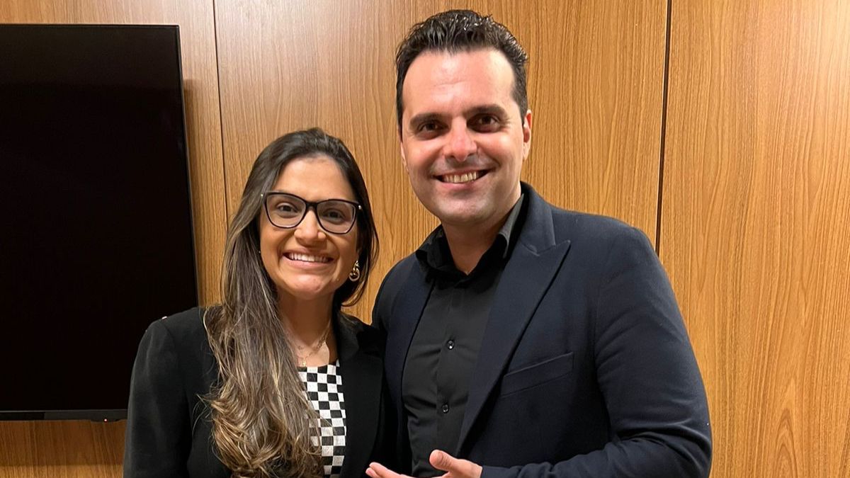 servidora Glacielle Torquato, jovem de cabelos longos, usa óculos, blazer escuro e blusa xadrez em preto e branco; com o palestrante Vitor Hugo Rocco, de blazer e camisa escura