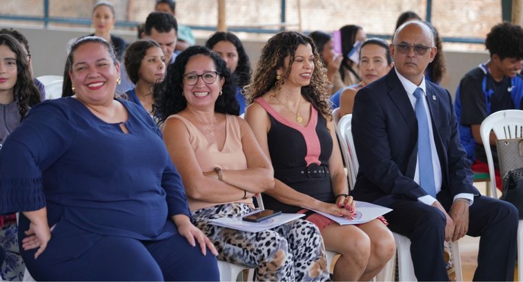 Mulheres sentadas em evento sorriem para foto