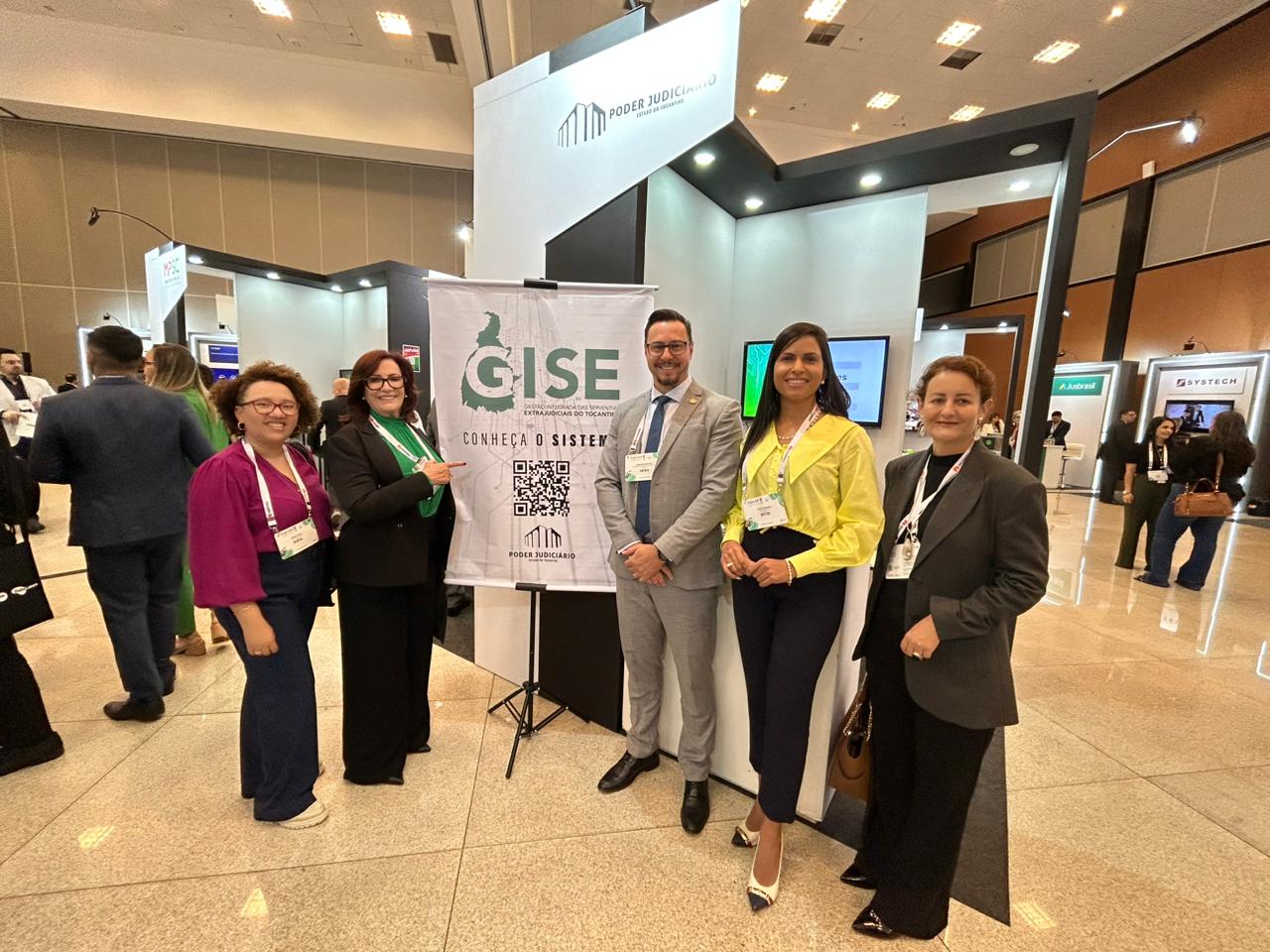 Mulheres e um homem posam para a foto em frente a um banner escrito GISE
