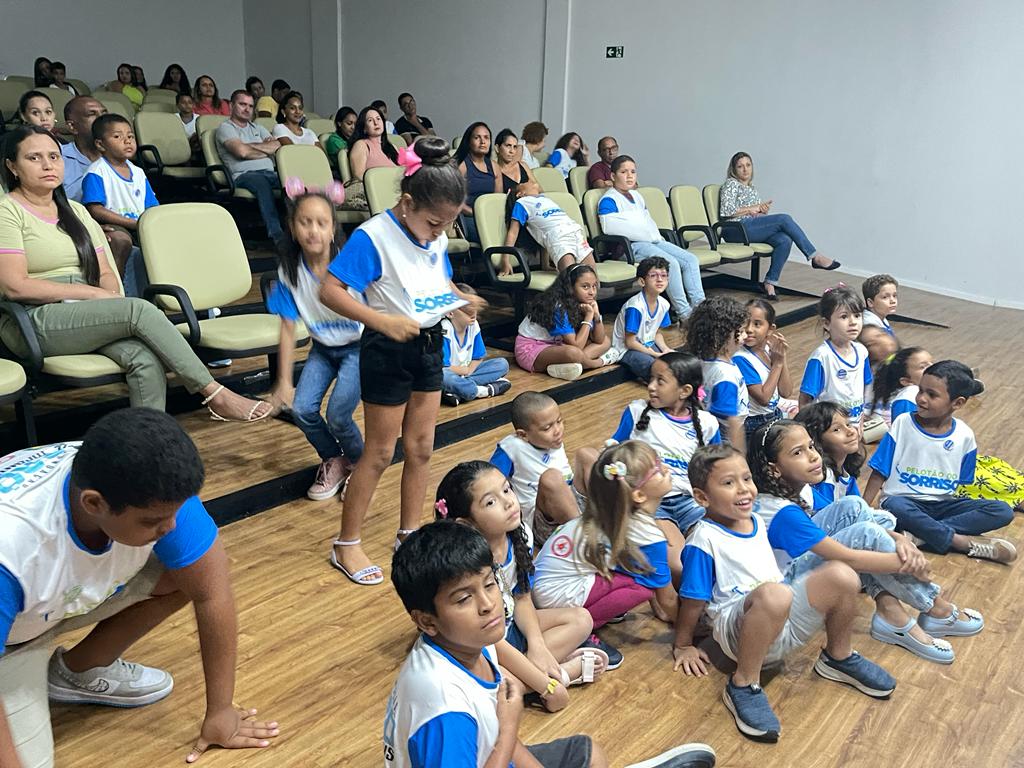 Várias crianças sentadas, uniformizadas, assistindo a um espetáculo teatral
