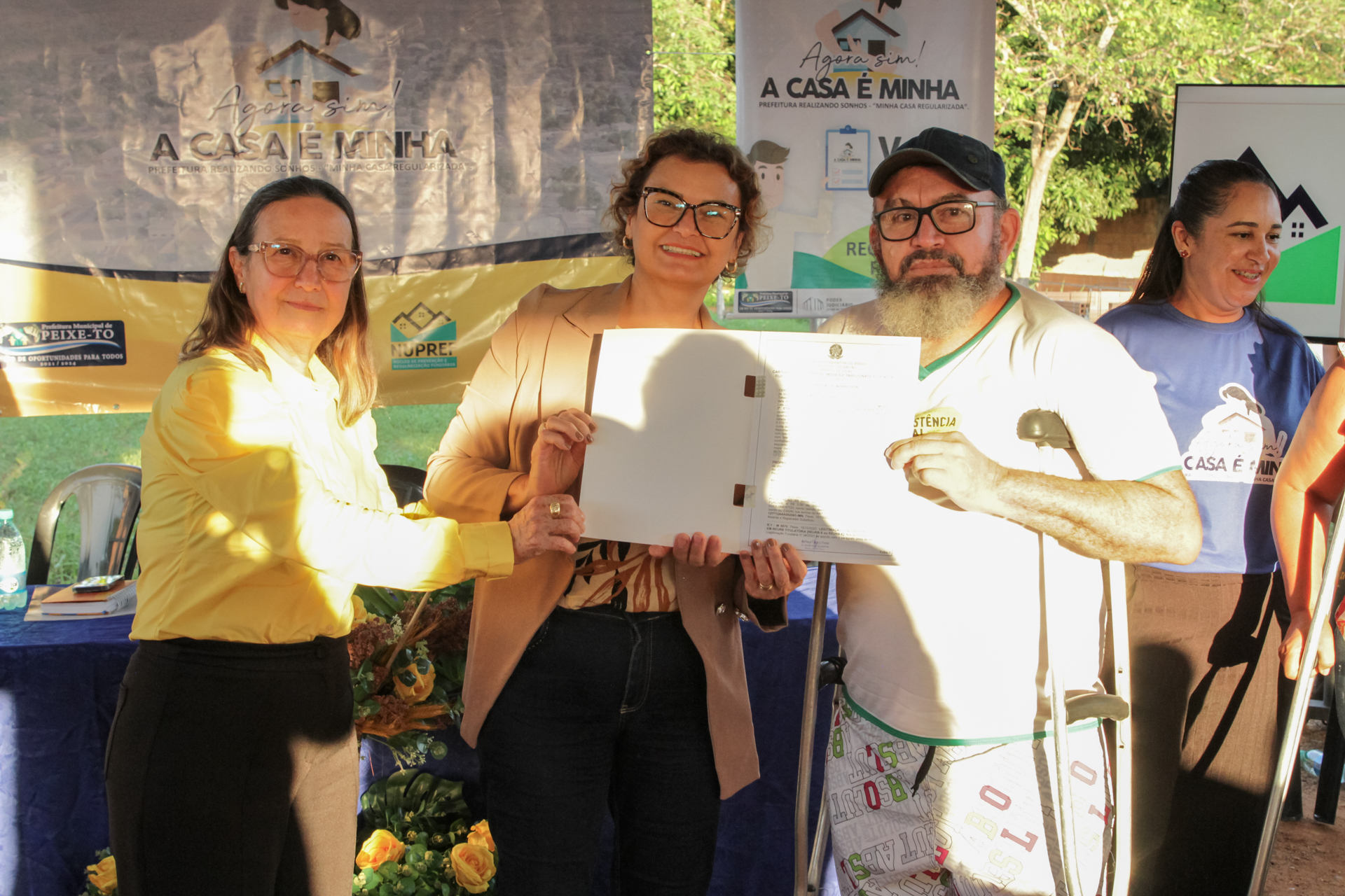 Duas mulheres e um homem seguram um documento de regularização fundiária