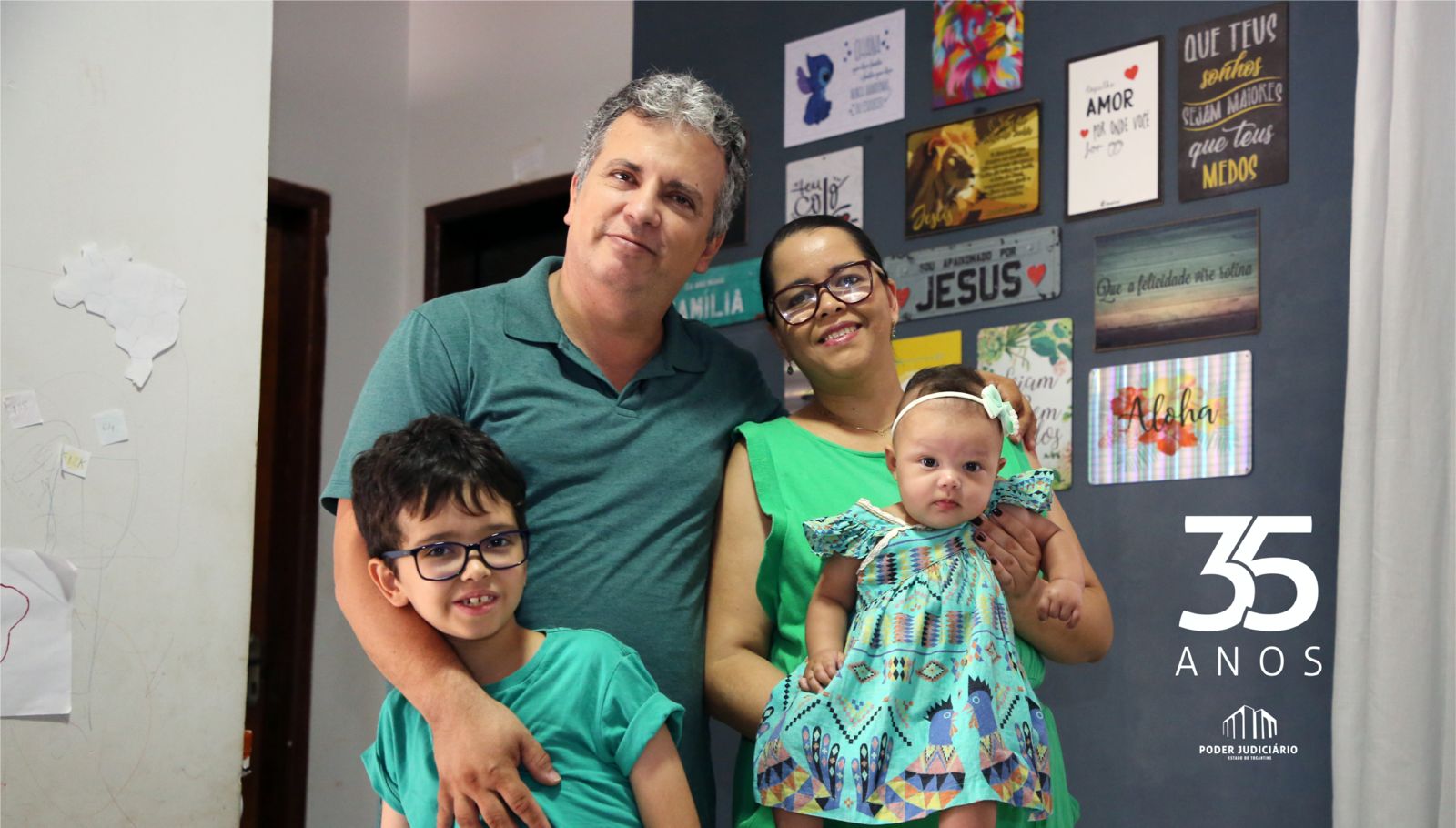 Imagem mostra dois adultos - um homem e uma mulher - uma criança e um bebê; todos usam roupas em tom de verde