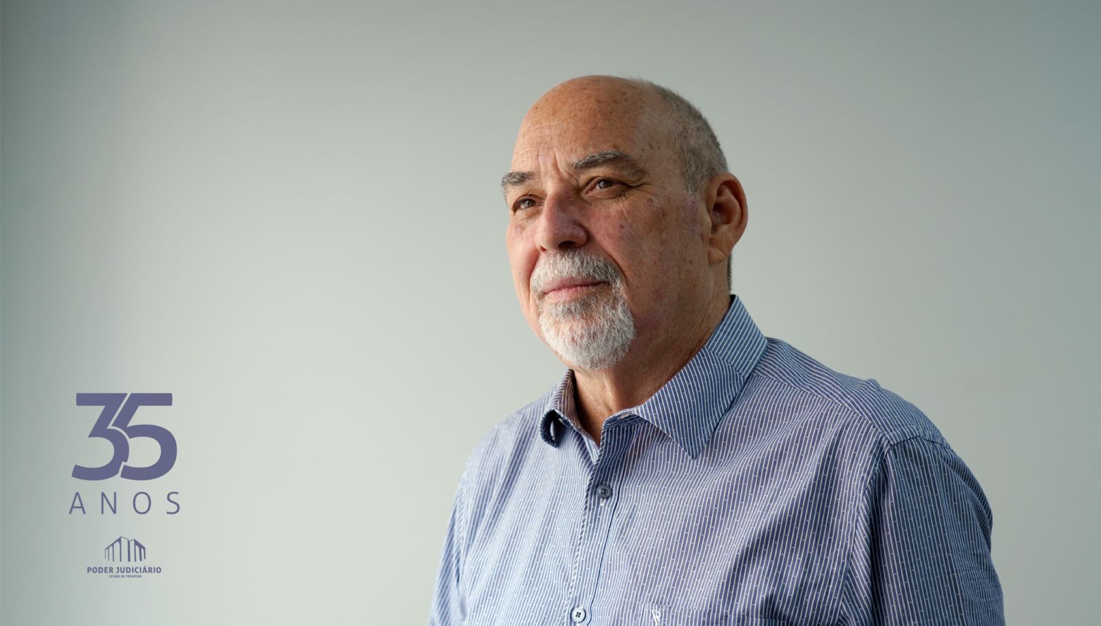 Foto de um homem branco, calvo, com barba branca e blusa azul