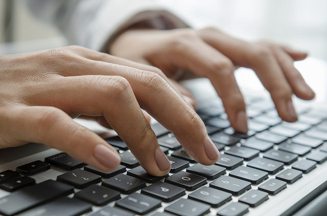 Fotografia colorida de mãos teclando em um teclado