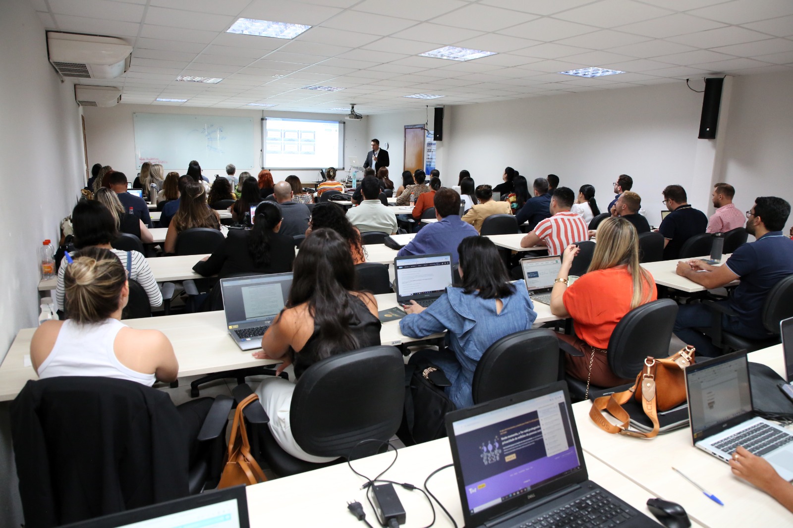 Fotografia colorida da capacitação sobre Sistemas Eletrônicos de Busca Patrimonial na Execução, com pessoas sentadas em cadeiras na plateia enquanto o professor palestra na frente