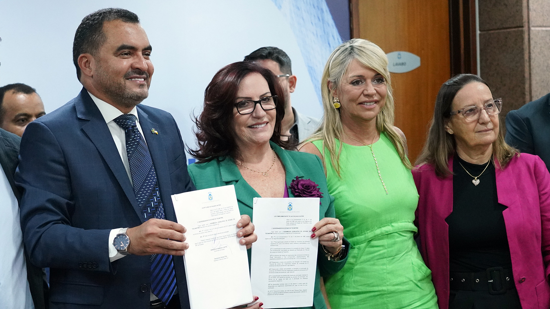 Imagem mostram quatro pessoas com roupas coloridas, em pé, segurando um papel que é uma lei