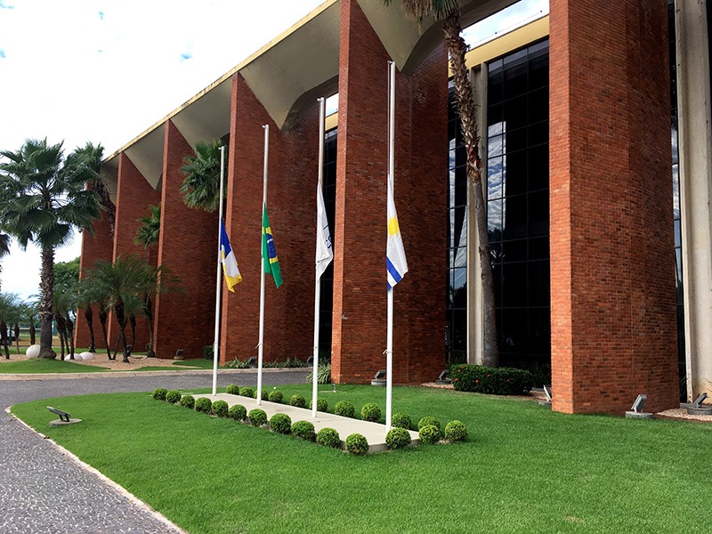 Fotografia colorida da frente do Tribunal de Justiça do Estado do Tocantins, onde se encontram as bandeiras do Tocantins, de Palmas, Brasil e Mercosul hasteadas a meio mastro como forma de homenagear o magistrado pelo seu trabalho e dedicação à magistratura tocantinense