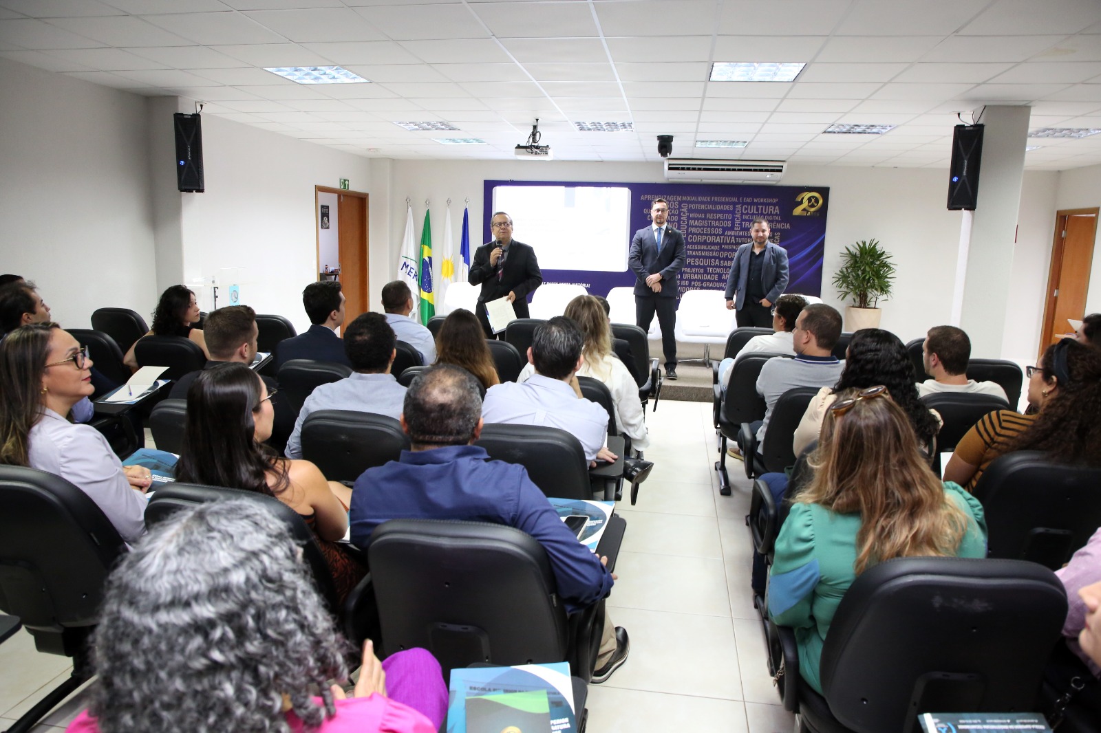 Fotografia colorida do curso para os delegatários aprovados no concurso público para o exercício notarial e registral. Os professores estão na frende da sala, ministrando a ula para os alunos que assistem sentados em suas cadeiras em sua frente.