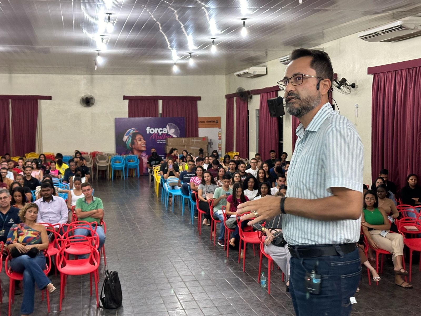 Um homem jovem, com barba e óculos, palestra para alunos da Unitins