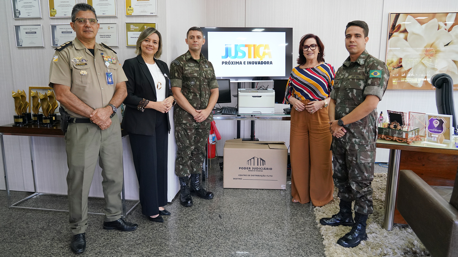 Imagem mostram cinco pessoas em pé, um militar PM, dois militares do exército fardados e duas mulheres, a presidente do TJTO e a diretora-geral do TJTO; todos posam para a foto
