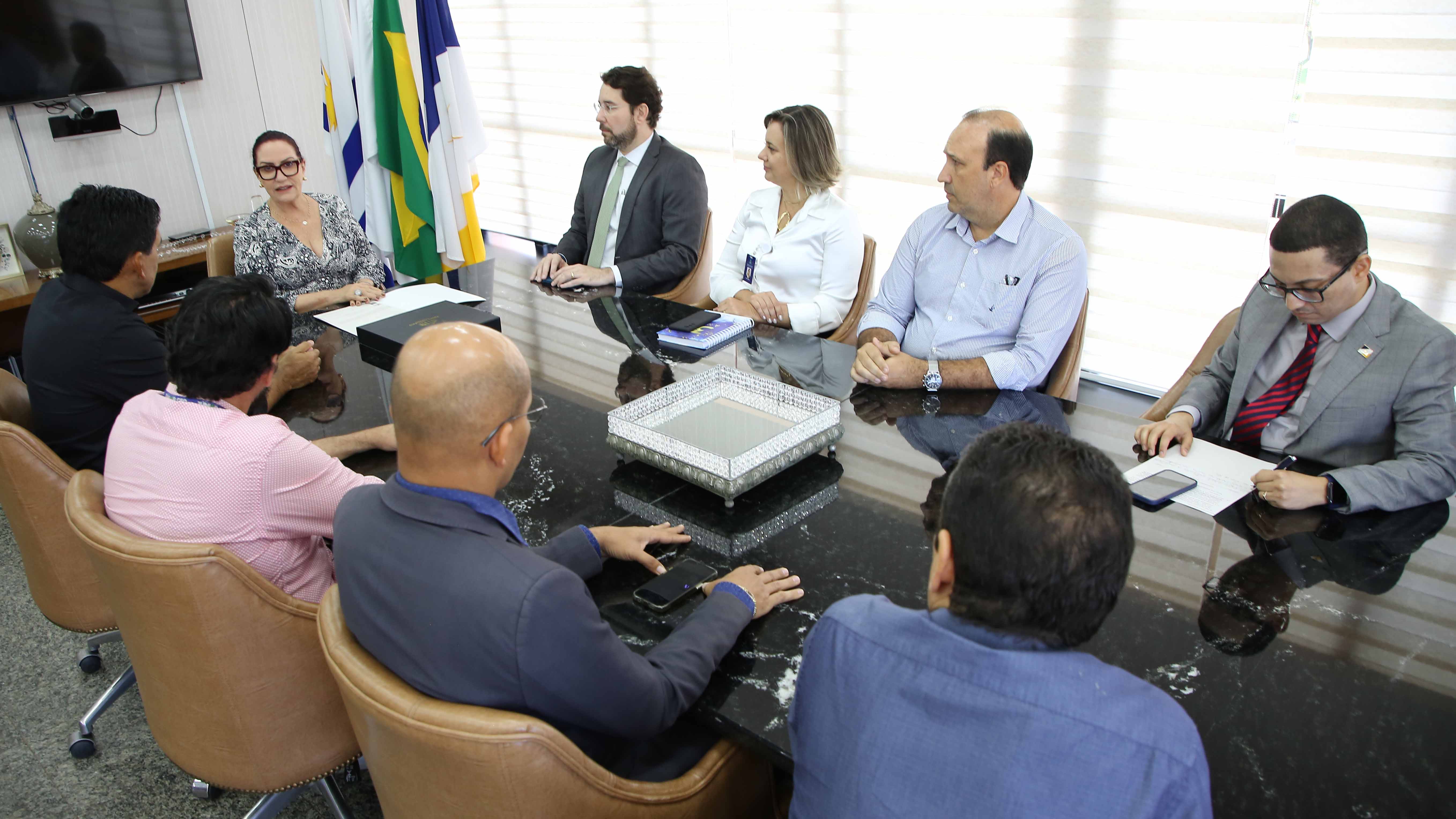 Imagem mostra homens e mulheres sentados em uma mesa durante uma reunião