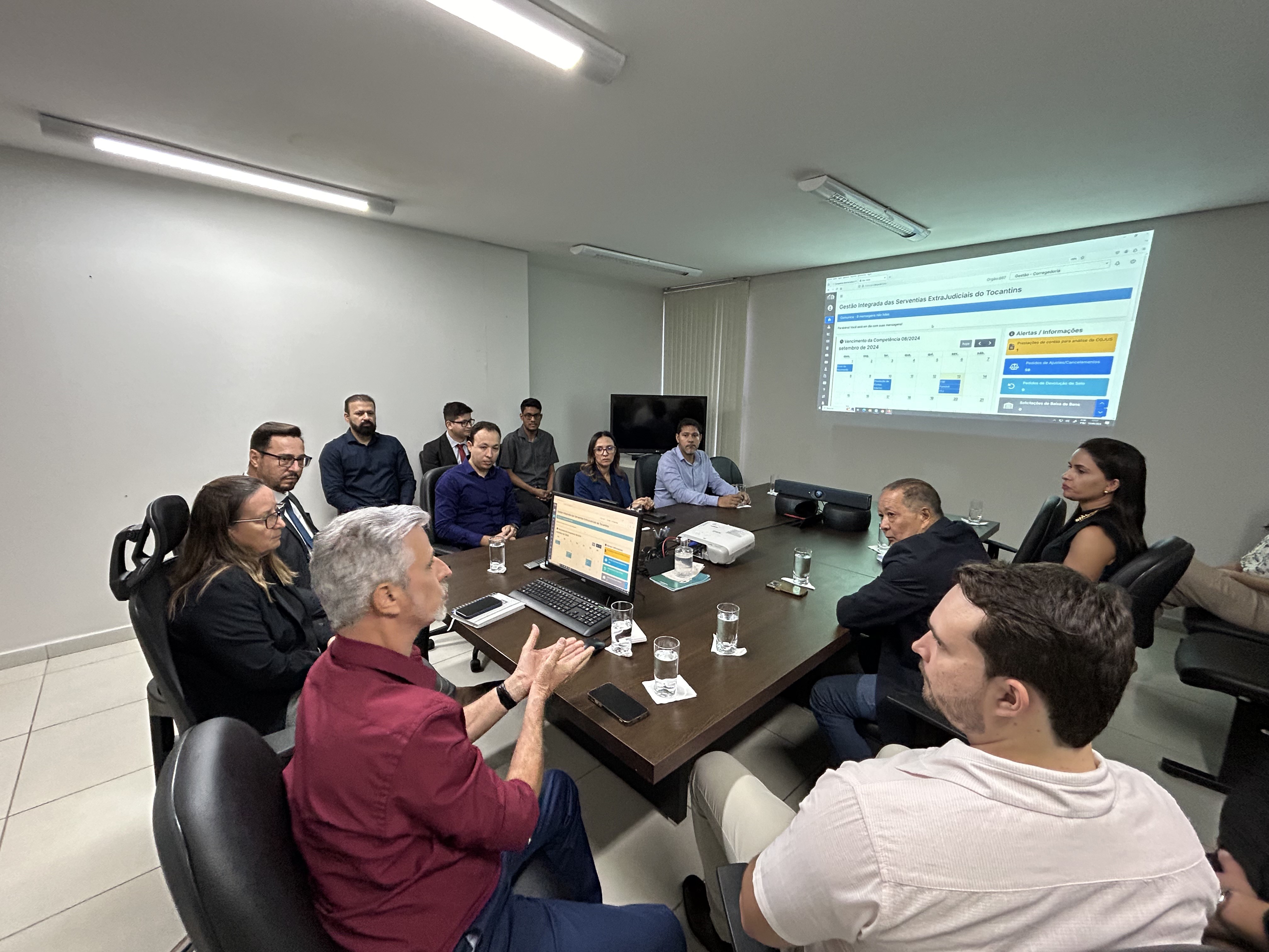Grupo de 12 pessoas reunidas sentadas ao redor de uma mesa prestando atenção ao que o orador da reunião está falando.